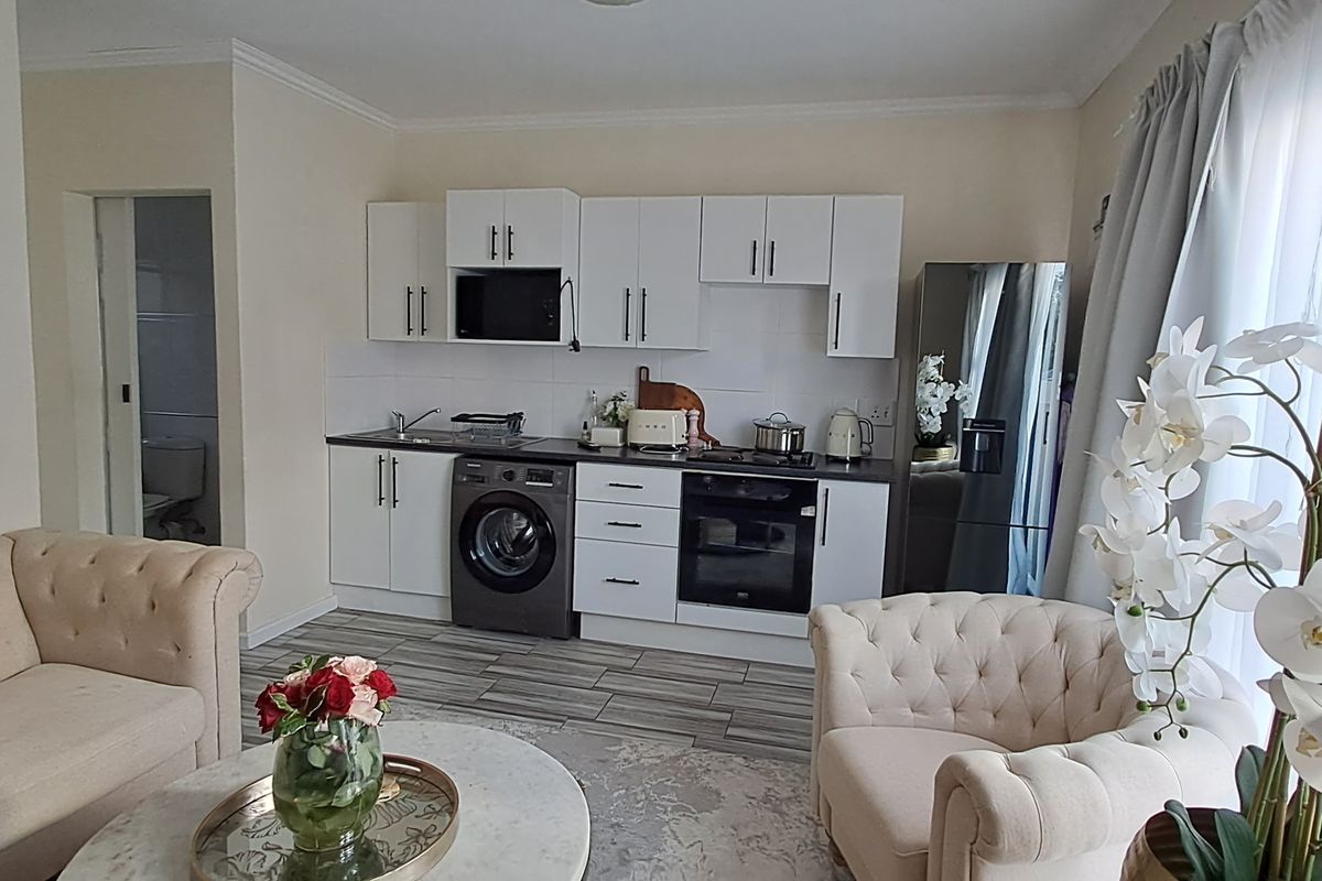 Open-plan living area featuring a modern kitchen with white cabinetry, integrated oven, and built-in laundry plumbing, seamlessly connected to the lounge space.