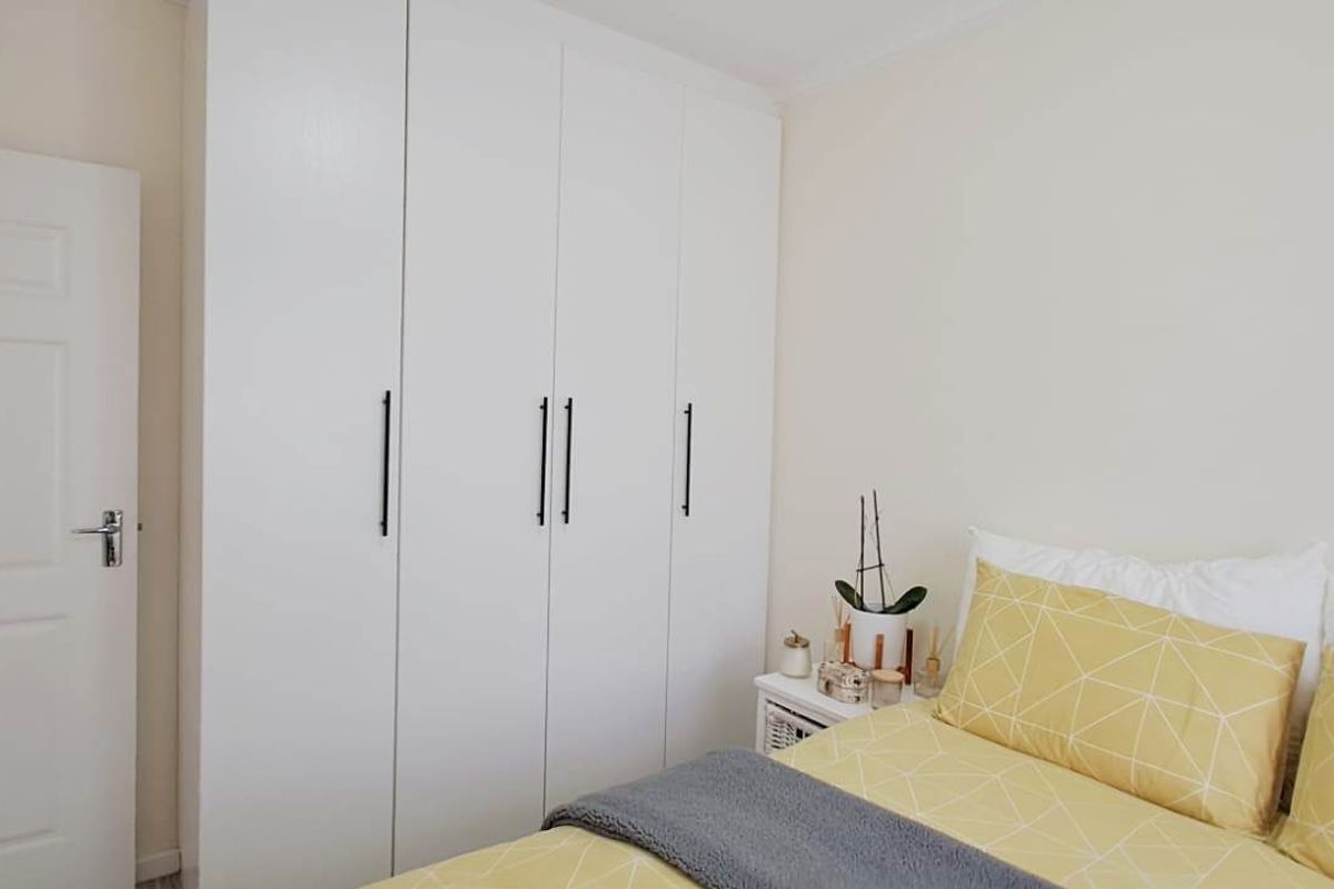 A bright bedroom featuring built-in floor-to-ceiling white cabinetry with modern black handles and a standard interior door.