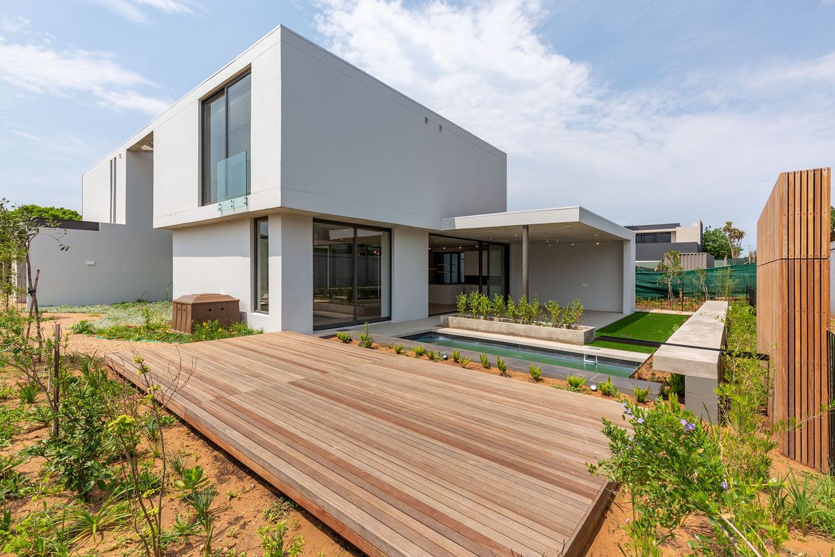 Modern architectural home featuring a timber deck, integrated lap pool, covered patio, and landscaped garden area.