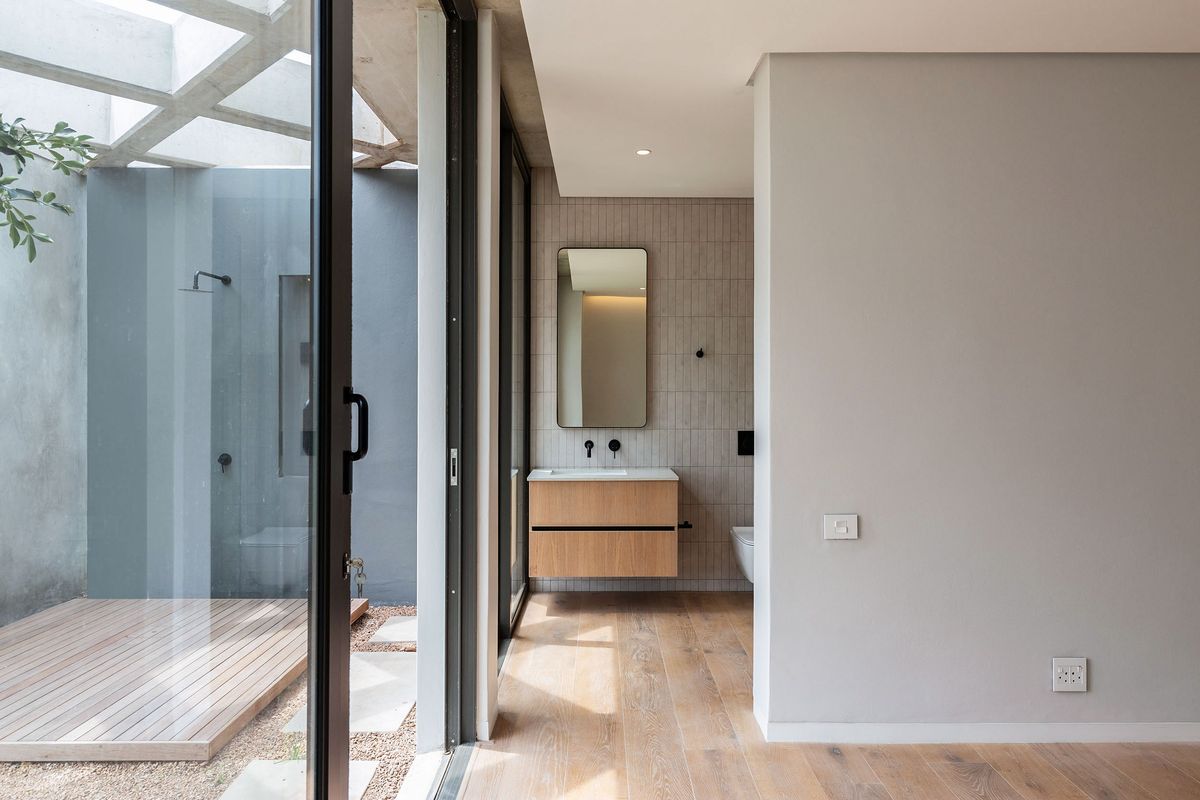 Modern bathroom featuring a floating vanity, wall-mounted mirror, and seamless transition to an outdoor shower area with timber decking and a glass enclosure.