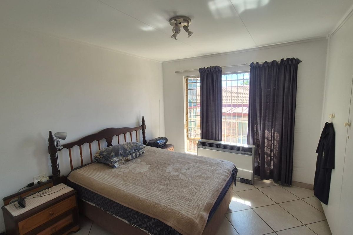 A bedroom featuring tiled flooring, built-in cupboards, and a window with security bars and curtains.