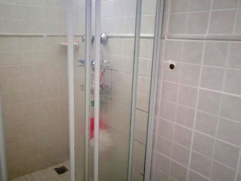 A dated bathroom shower enclosure featuring tiled walls and flooring, requiring cosmetic updates and maintenance to the fixtures and grout.
