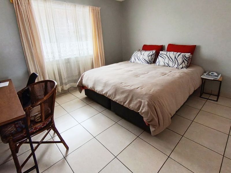 A functional bedroom featuring neutral tiled flooring and a large window with installed curtain rails, providing a clean and simple living space.