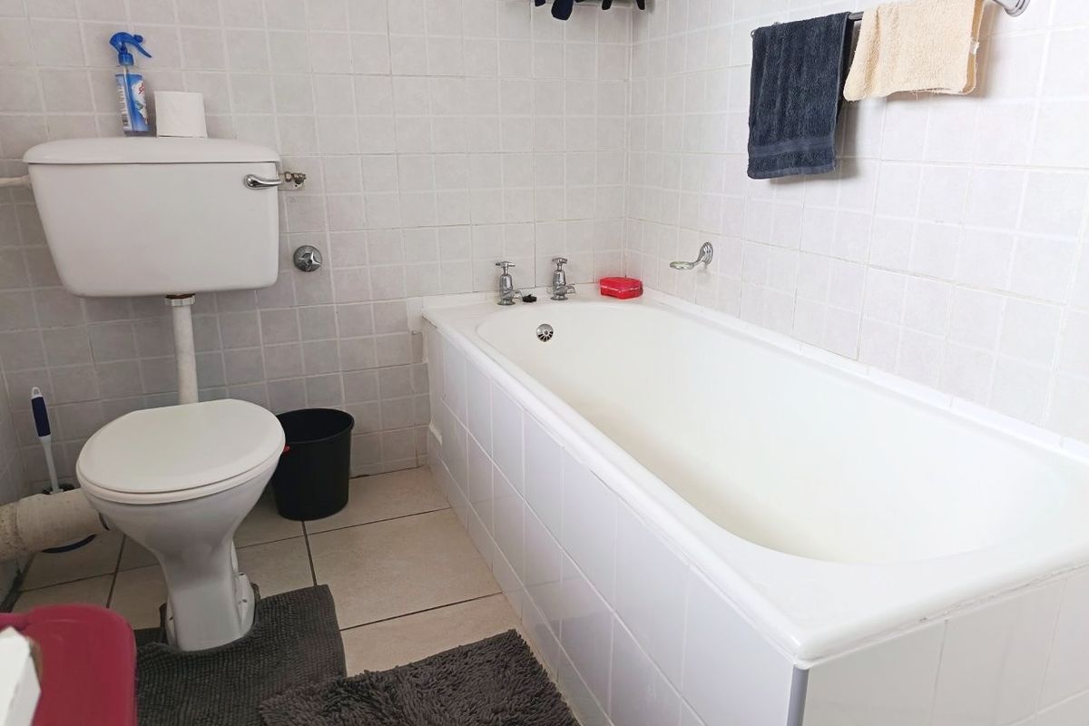 A functional bathroom featuring a standard bathtub and toilet with white wall tiling and tiled flooring, presenting an opportunity for modernization.
