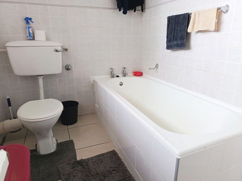 A functional bathroom featuring a standard bathtub and toilet with white wall tiling and tiled flooring, presenting an opportunity for modernization.