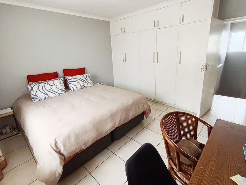 A functional bedroom featuring neutral tiled flooring and extensive white built-in cupboards providing ample storage space.