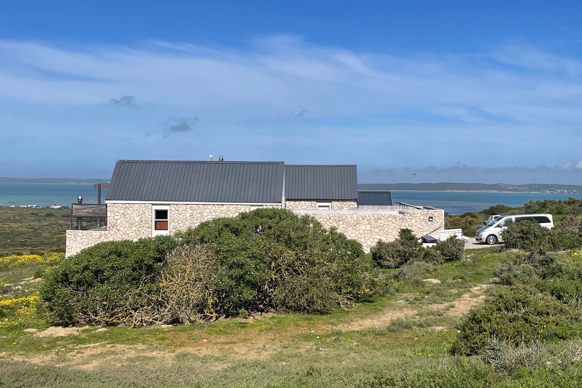 A view of the rear elevation of a stone-clad residence featuring a metal roof, set within a natural coastal landscape with water views.