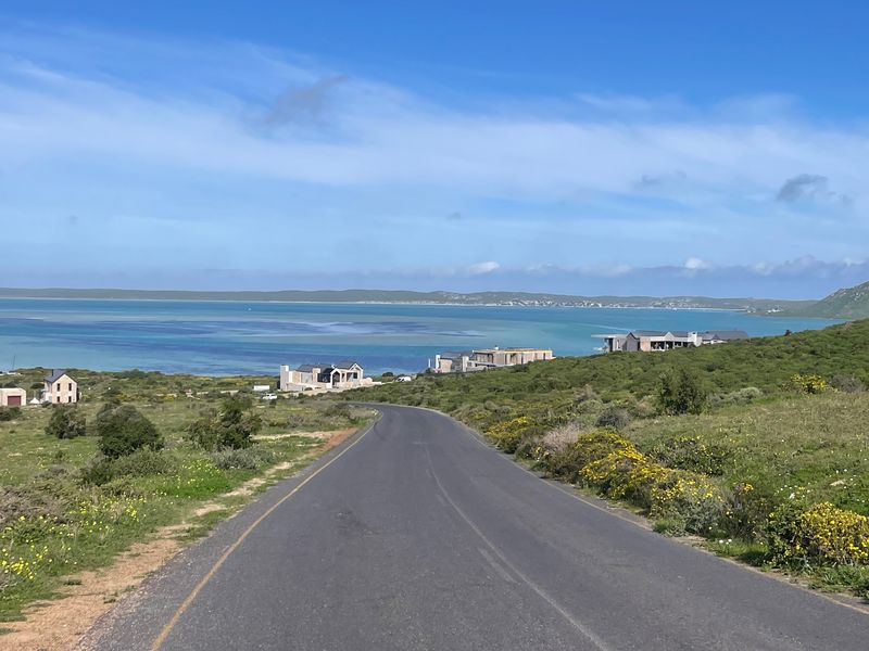 A scenic view of a coastal road leading towards the ocean, surrounded by natural landscape and nearby residential properties.
