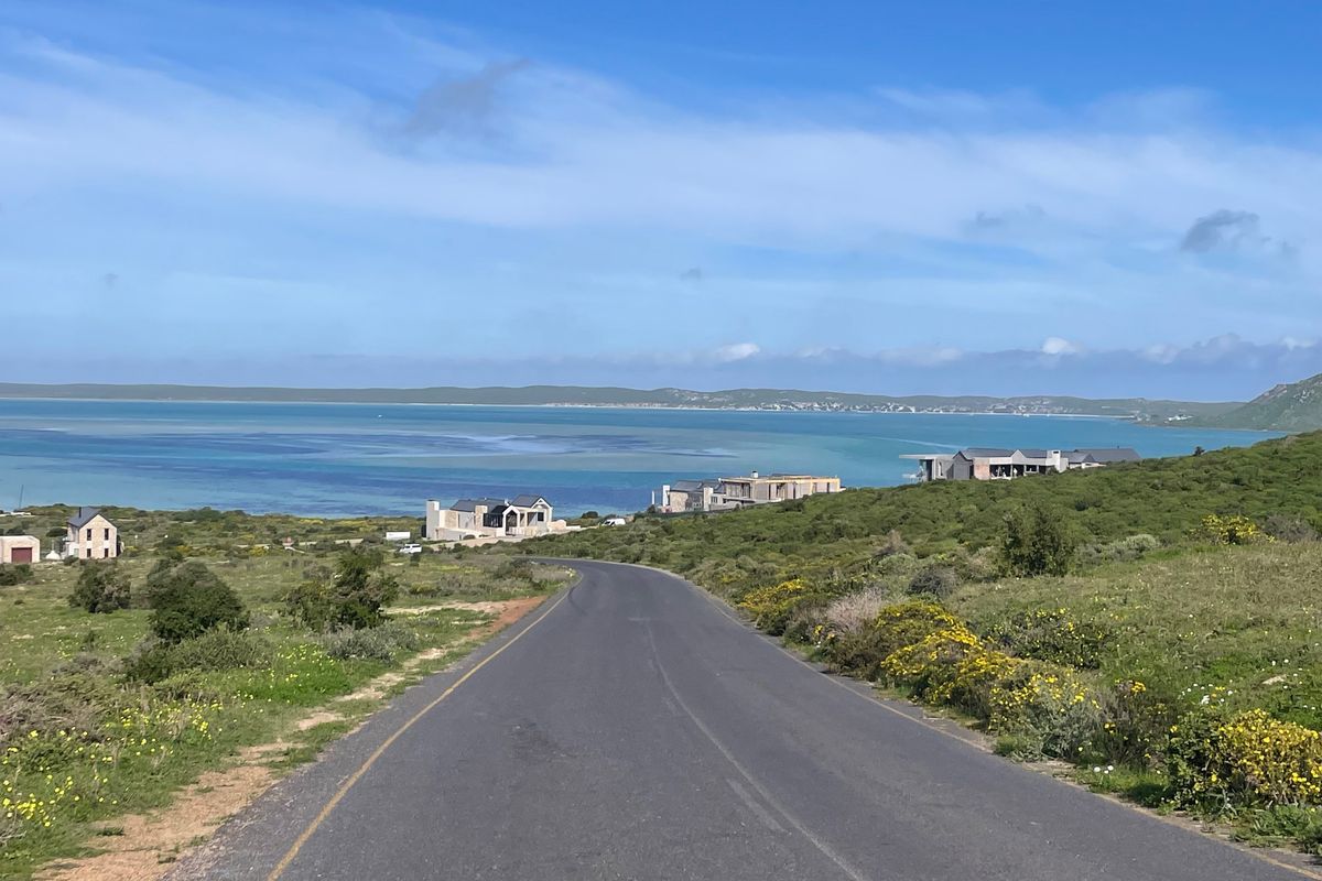 A scenic view of a coastal road leading towards the ocean, surrounded by natural landscape and nearby residential properties.