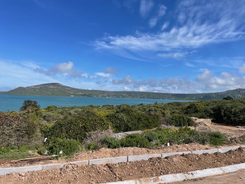 A scenic view of the lagoon and surrounding hills from the vacant residential plot, featuring natural coastal vegetation and established boundary curbing.
