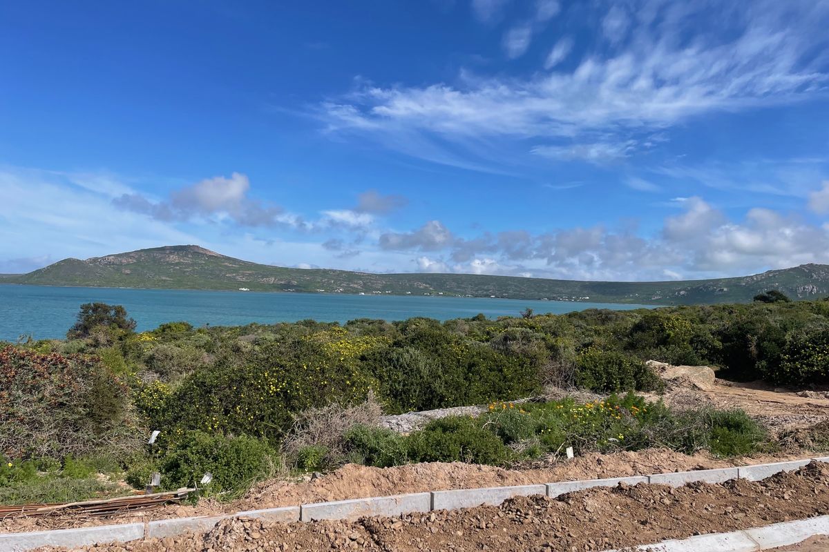 A scenic view of the lagoon and surrounding hills from the vacant residential plot, featuring natural coastal vegetation and established boundary curbing.