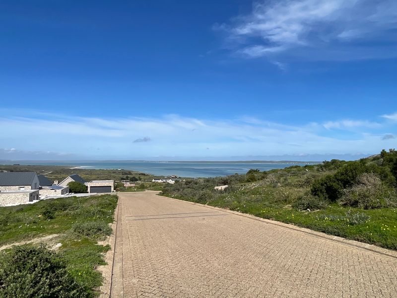 A view looking down a paved residential street towards the coastal landscape and ocean in the distance.