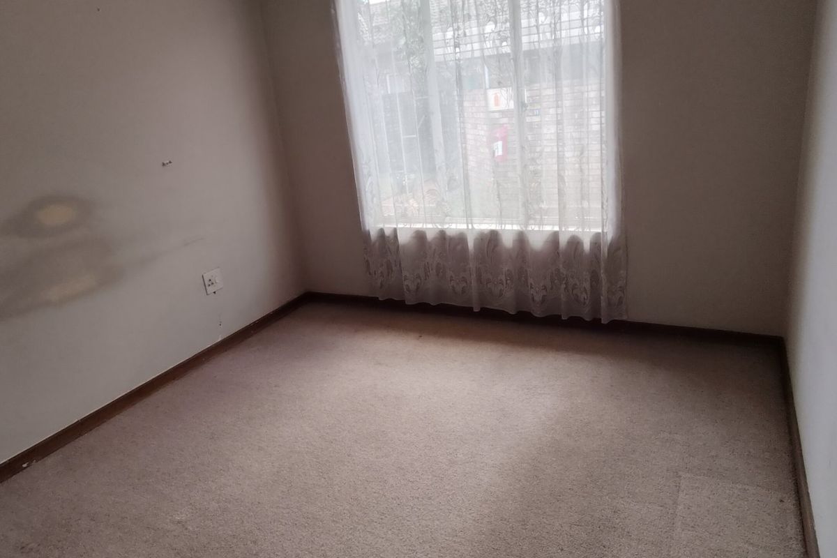 An empty bedroom featuring neutral carpeting and a large window, requiring cosmetic updates to the walls and flooring.