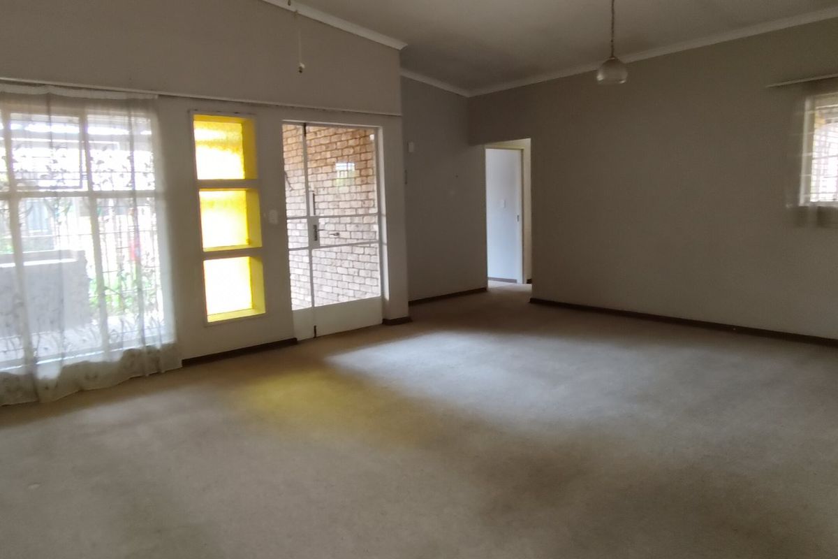 A spacious, empty living area featuring neutral walls, carpeted flooring, and large windows providing natural light, ready for a modern update.