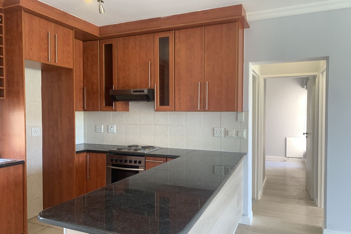 A functional kitchen featuring cherry wood cabinetry, granite countertops, a breakfast bar, and built-in cooking appliances, leading into a hallway.