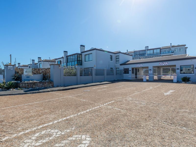 Front entrance view of the apartment complex featuring a secure gated access point, paved driveway, and perimeter wall with electric fencing.