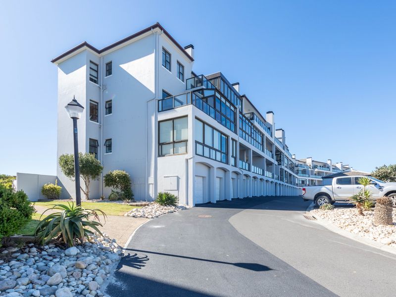 Exterior view of a modern multi-story apartment complex featuring balconies, paved driveway, and landscaped garden areas.