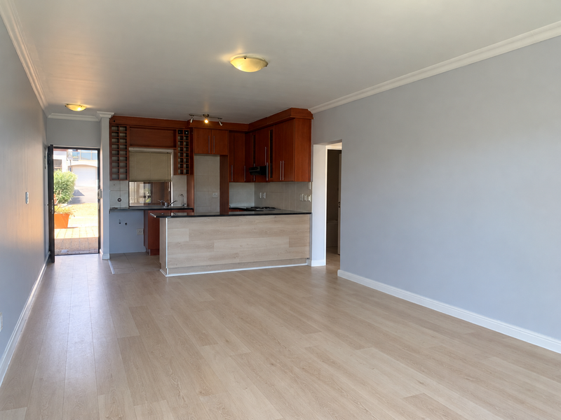 Spacious open-plan living area featuring light laminate flooring and a functional kitchen with wood-finish cabinetry, granite countertops, and integrated extractor fan.