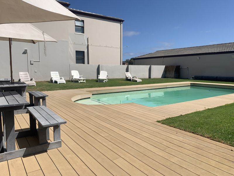 A well-maintained outdoor pool area featuring timber decking, a clear swimming pool, and a surrounding lawn with boundary walling.