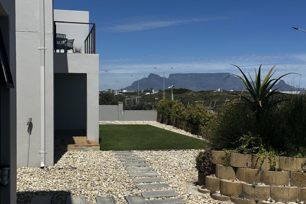 A well-maintained rear garden featuring an artificial lawn, stone pathway, and a balcony with mountain views.