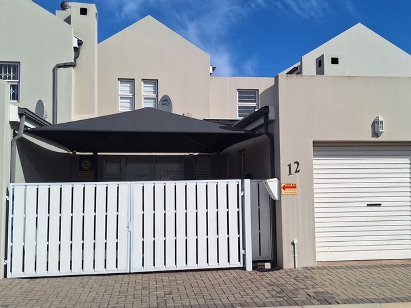 Front elevation of a residential property featuring a paved driveway, double garage, secure white gate, and a shaded entrance area.