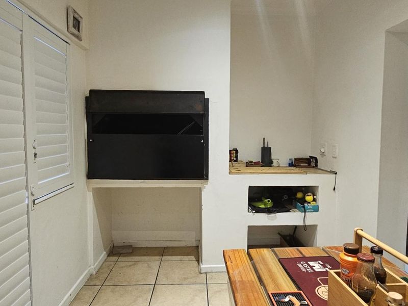 Covered patio area featuring a built-in braai, tiled flooring, and shutter blinds, providing a functional space for outdoor entertaining.