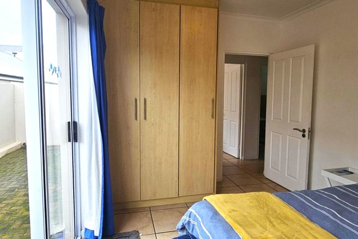 Bedroom featuring built-in wooden wardrobes, tiled flooring, and a sliding glass door providing direct access to an outdoor paved area.