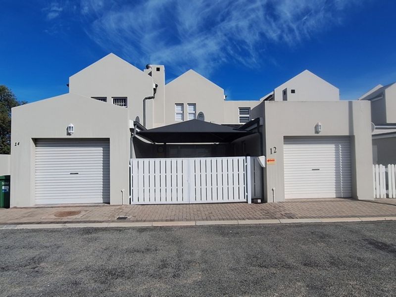 Front elevation of a modern residential property featuring dual garage doors, paved driveway, and secure gated entrance.