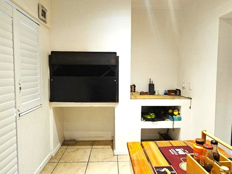 Covered patio area featuring a built-in braai, tiled flooring, and shutter blinds, providing a functional space for outdoor entertaining.