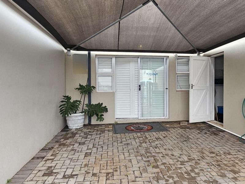 A paved outdoor patio area featuring a shade sail, sliding glass door access, and a stable door leading into the home.