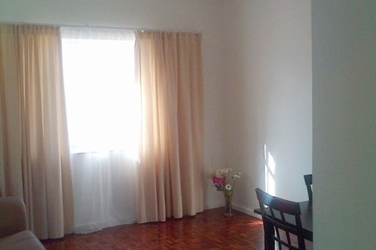 A living room area featuring classic parquet flooring and natural light through a window with curtains.