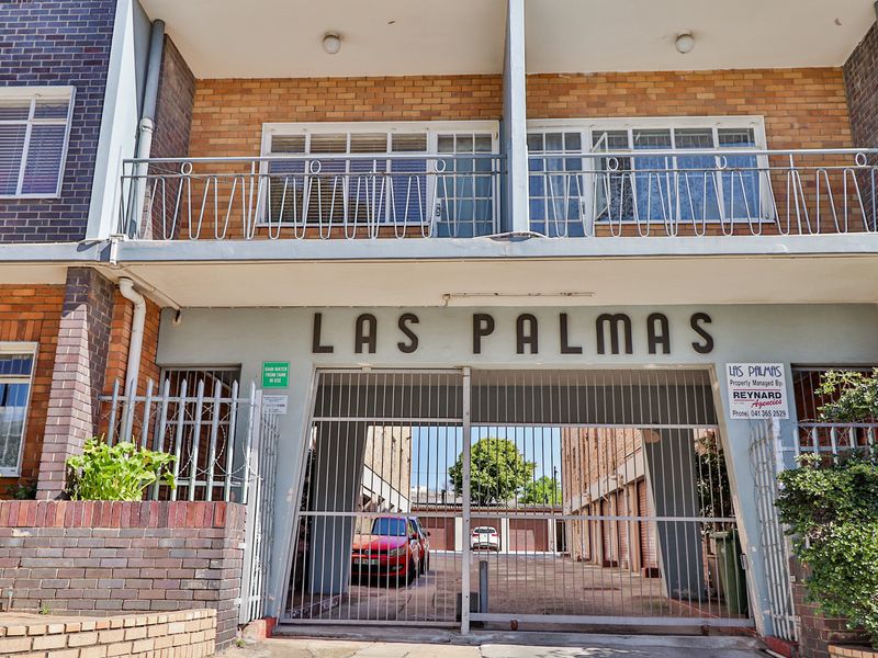 Front elevation of Las Palmas apartment complex featuring a secure gated entrance, brick facade, and upper-level balconies with metal railings.