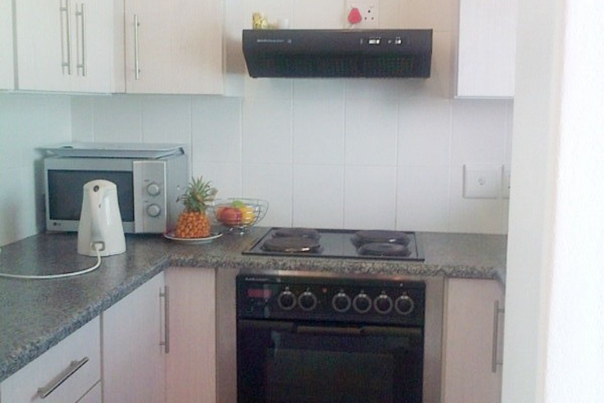 A compact kitchen featuring white cabinetry, granite-look laminate countertops, a built-in oven with electric hob, and an extractor fan.