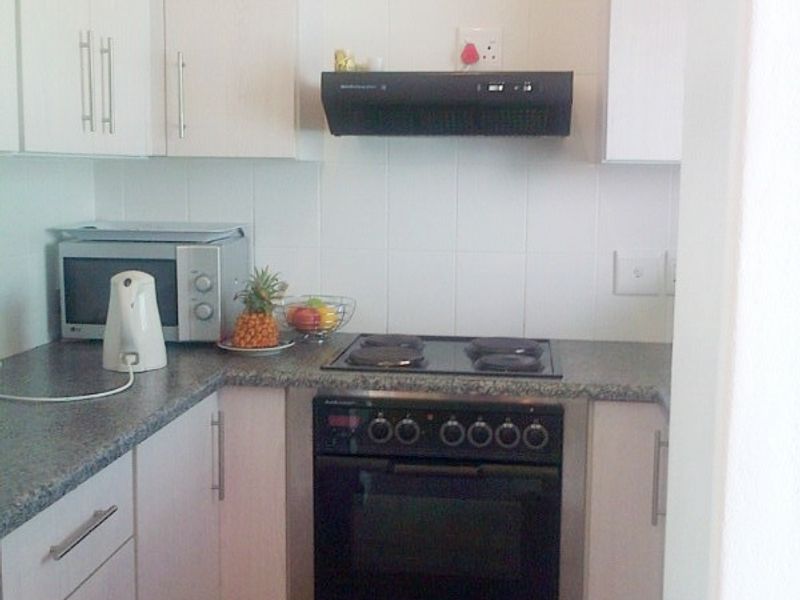 A compact kitchen featuring white cabinetry, granite-look laminate countertops, a built-in oven with electric hob, and an extractor fan.