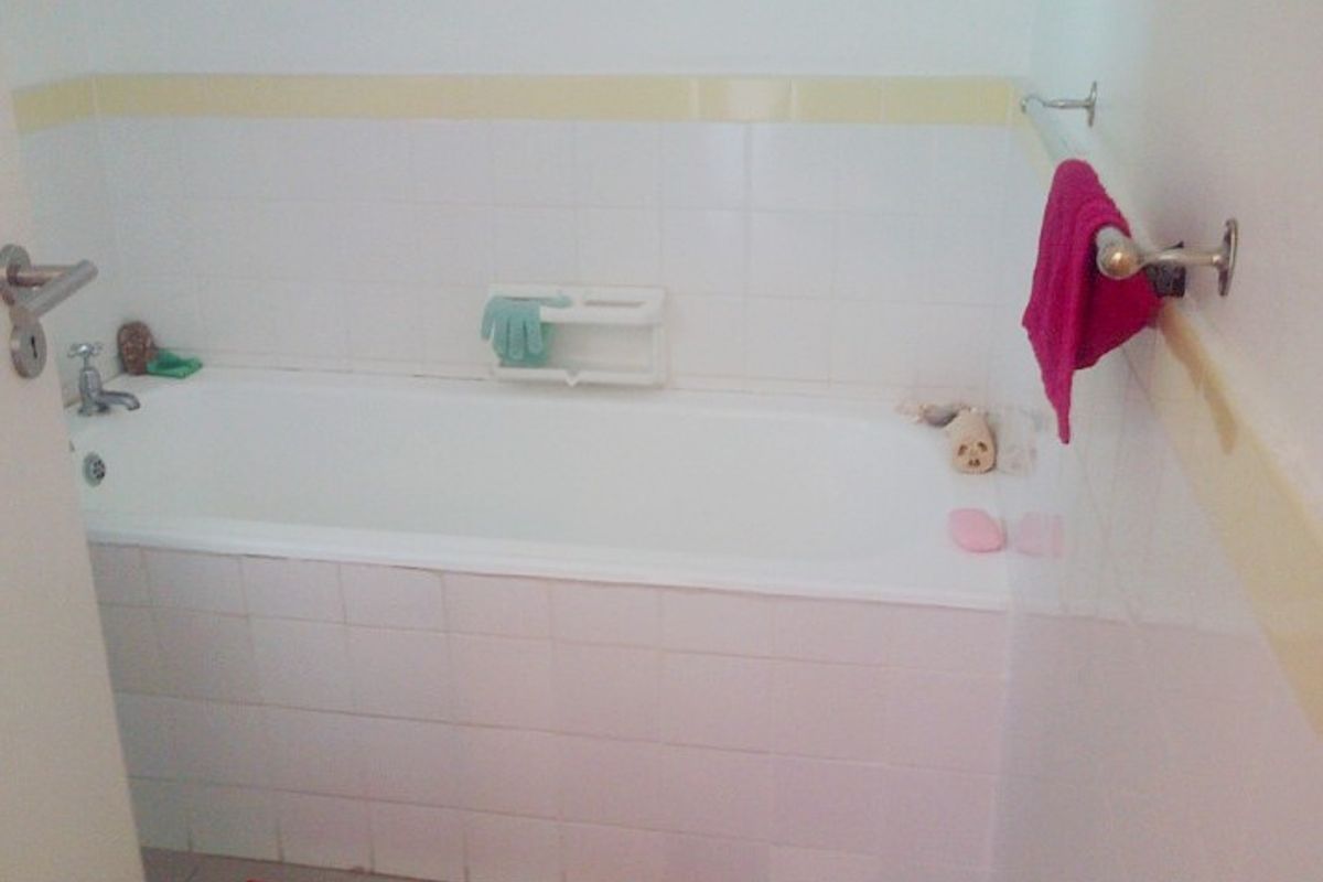 A functional bathroom featuring a standard bathtub with white wall tiling and a chrome towel rail.