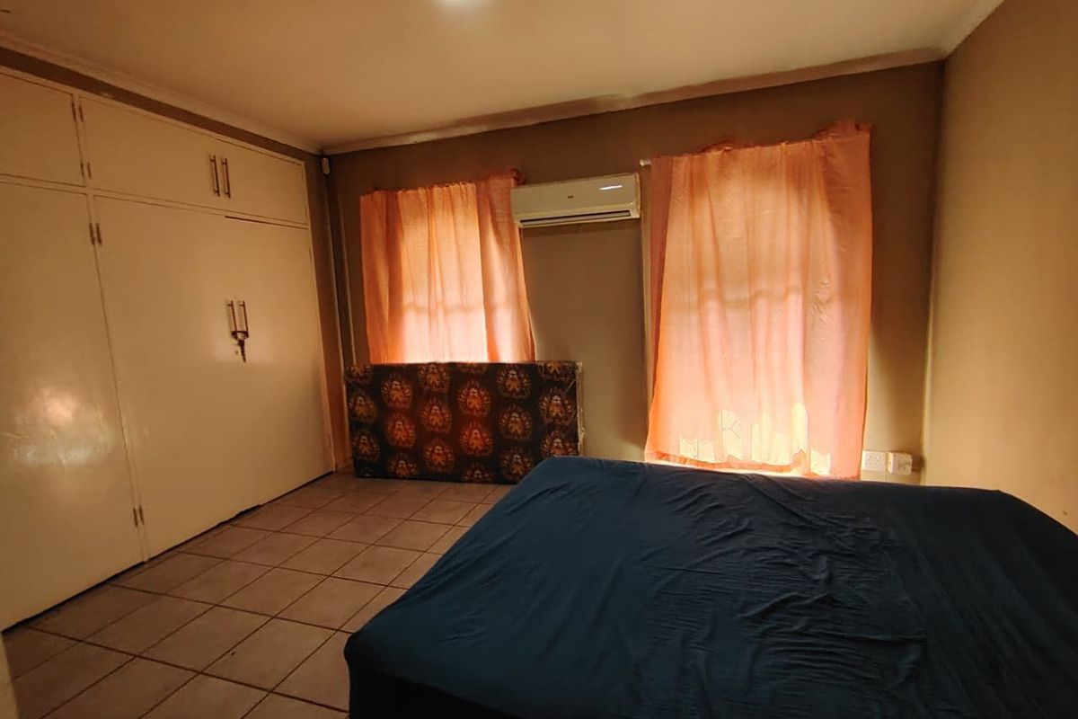 A bedroom featuring built-in cupboards, tiled flooring, and a wall-mounted air conditioning unit.