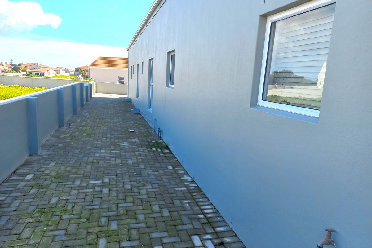 A side exterior walkway featuring paved flooring, a boundary wall, and an outdoor water tap along the side of the house.