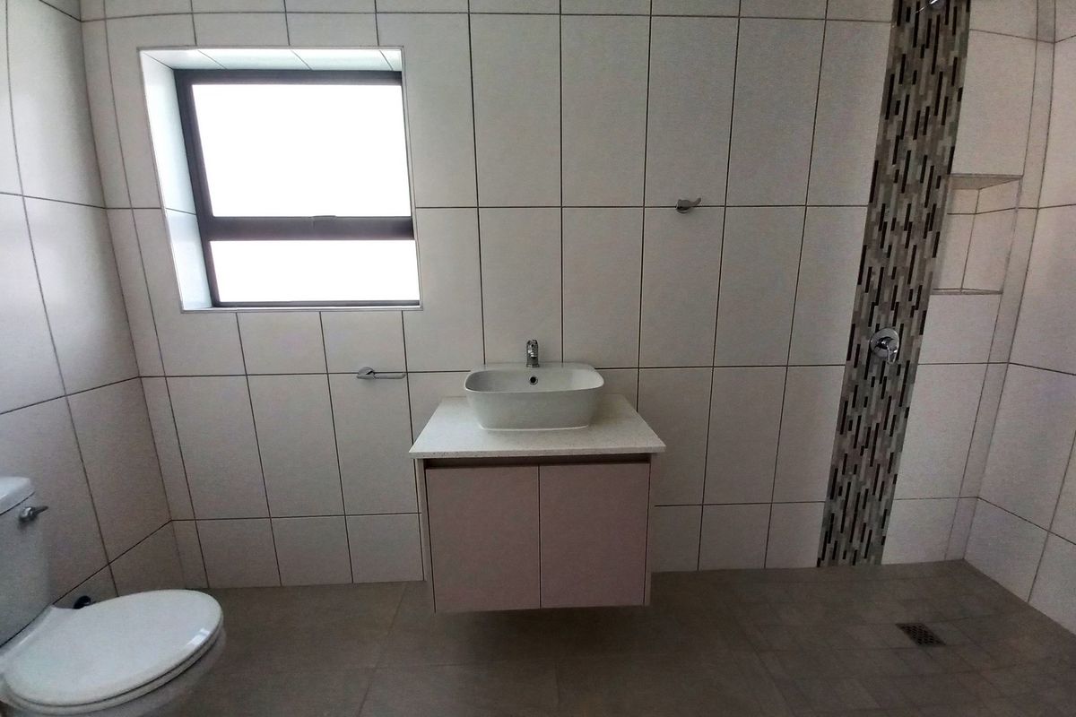 Modern bathroom featuring a wall-mounted vanity with vessel sink, walk-in shower with mosaic tile accent, and neutral floor-to-ceiling wall tiling.