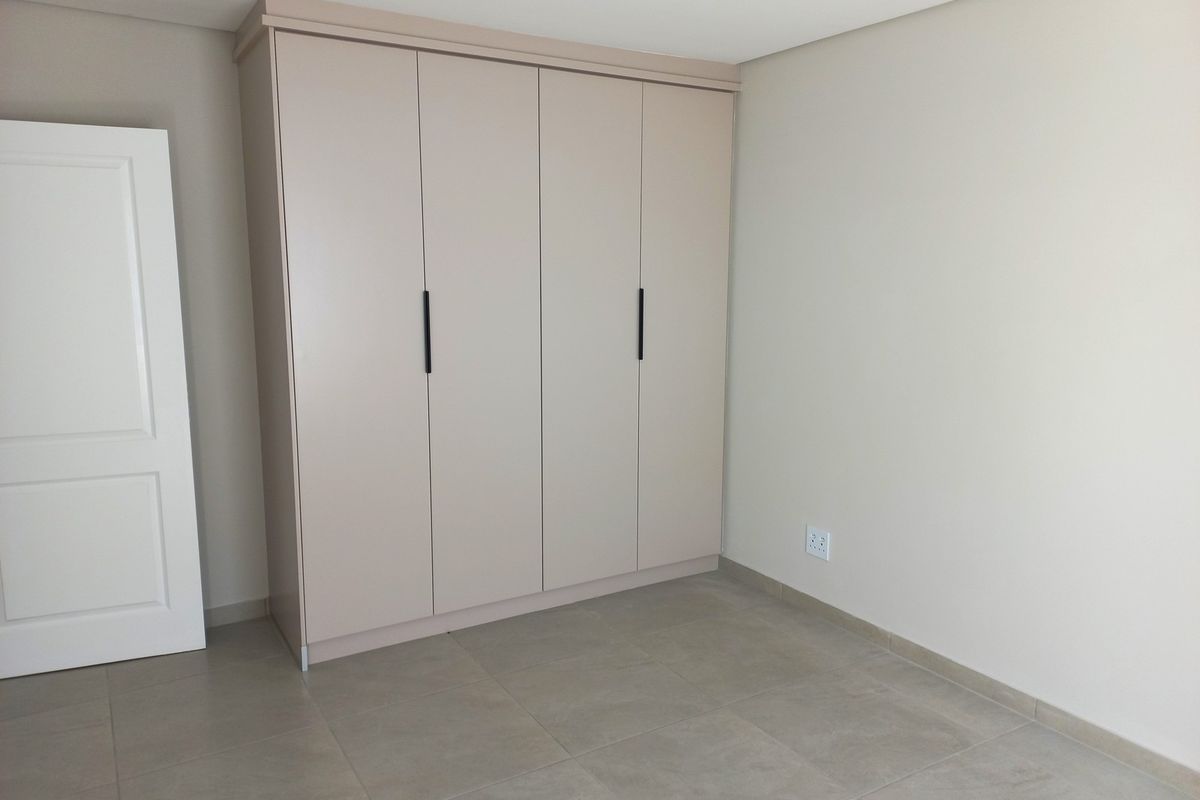 A clean, modern bedroom featuring neutral-toned floor tiles and a large, built-in wardrobe with sleek, contemporary handles.