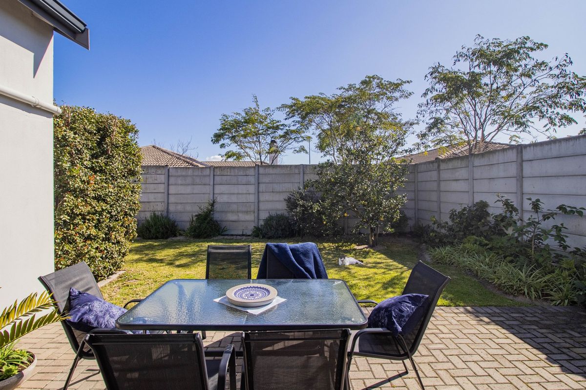 A private rear garden featuring a paved patio area, established lawn, and secure precast concrete boundary walls.