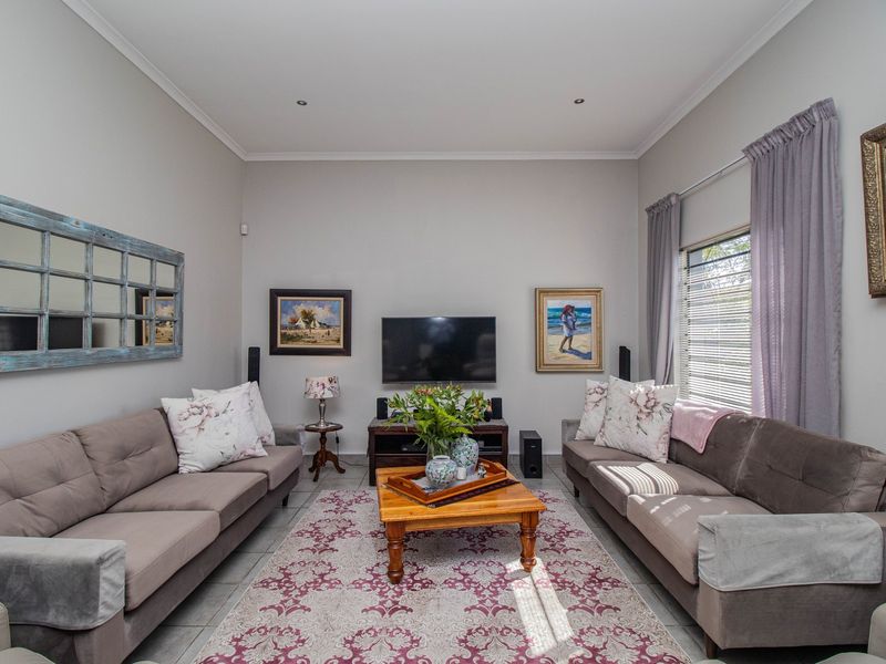 A well-maintained living room featuring neutral wall tones, tiled flooring, recessed downlighting, and large windows fitted with venetian blinds.