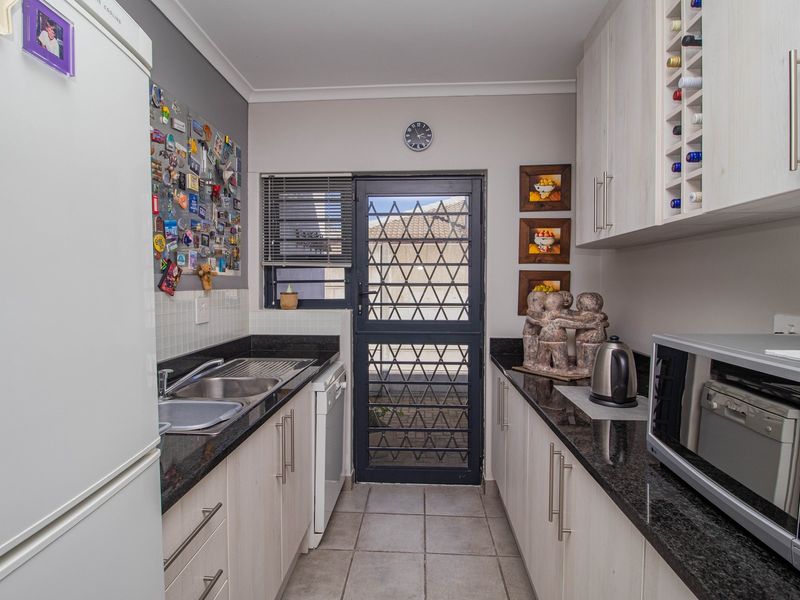 A functional scullery featuring granite countertops, ample built-in cabinetry with integrated wine storage, a double sink, and direct access to the exterior via a security gate.