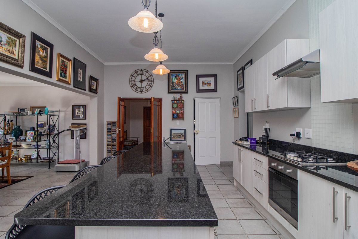 Modern kitchen featuring a large granite island, built-in oven, gas hob, extractor fan, and ample cabinetry, seamlessly flowing into the adjacent living area.