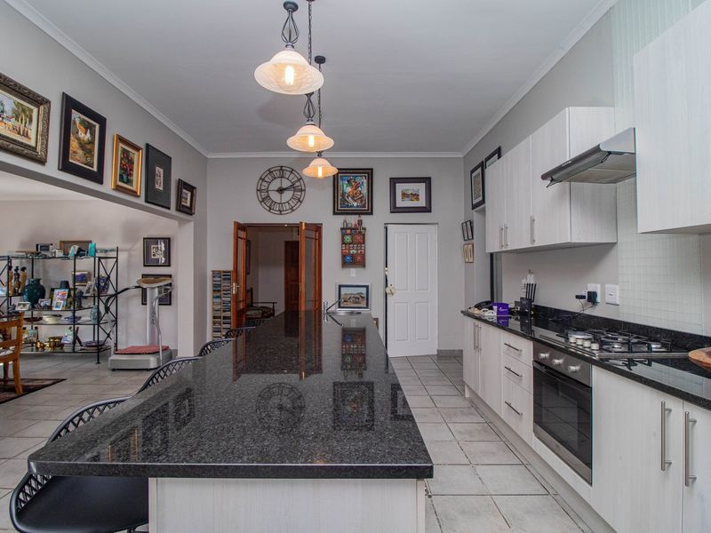 Modern kitchen featuring a large granite island, built-in oven, gas hob, extractor fan, and ample cabinetry, seamlessly flowing into the adjacent living area.