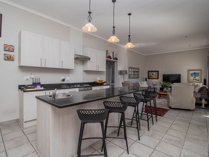 Open-plan kitchen and living area featuring light-toned cabinetry, granite countertops, a central island with breakfast bar, and modern pendant lighting.