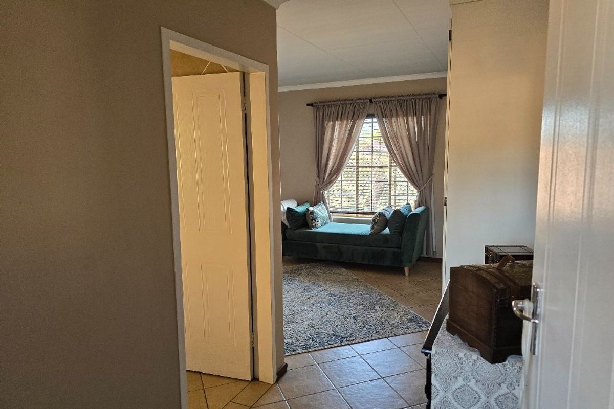A view from a hallway looking into a bedroom featuring tiled flooring, a window with curtains, and a doorway leading to an adjacent space.