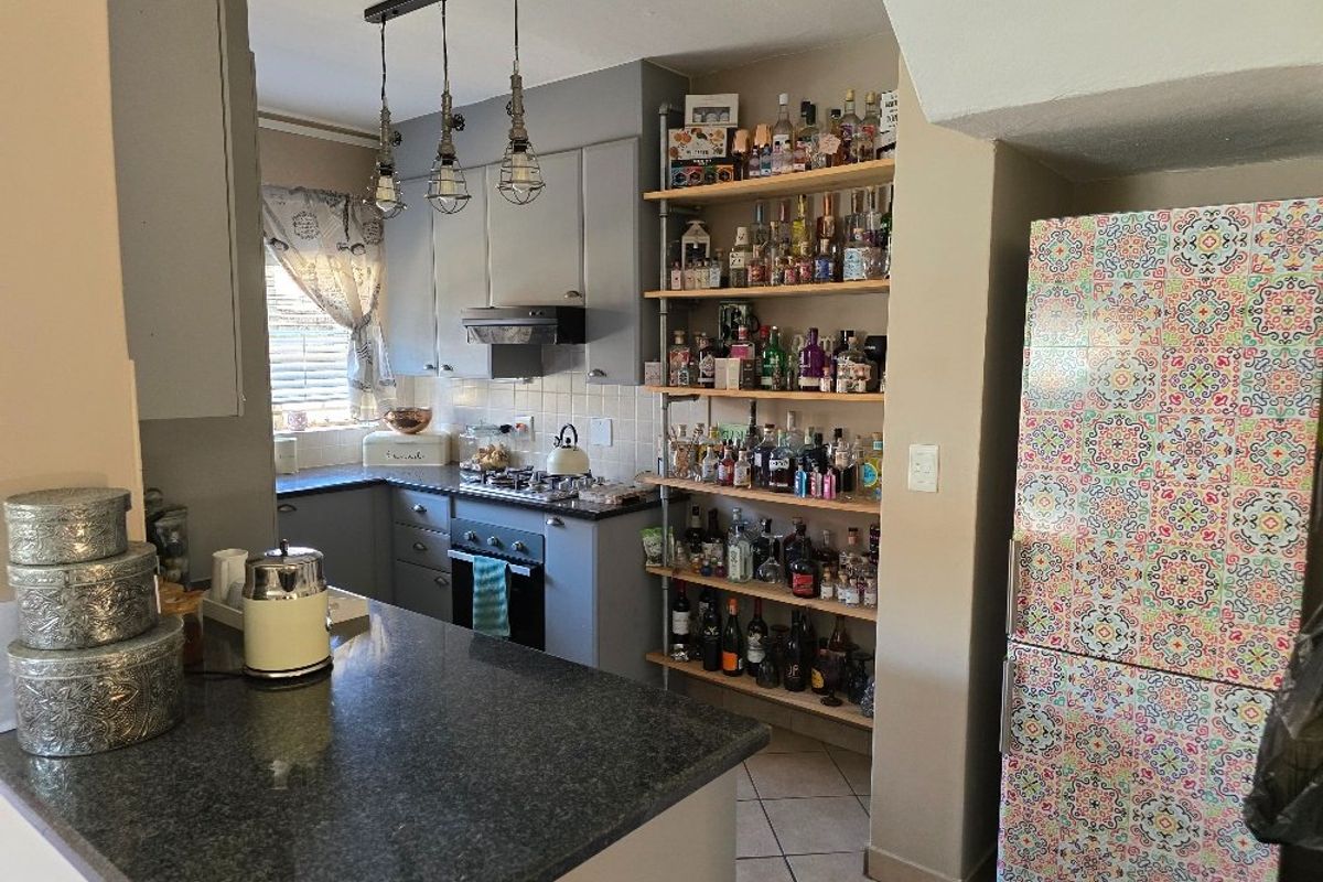 A compact kitchen featuring grey cabinetry, granite countertops, a built-in hob and extractor fan, and open shelving for storage.