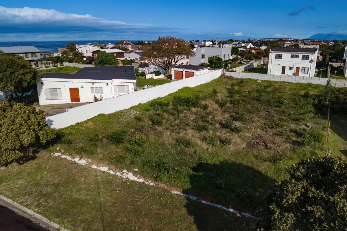 Aerial view of a vacant residential plot featuring established boundary walls and proximity to local neighborhood infrastructure and coastal views.