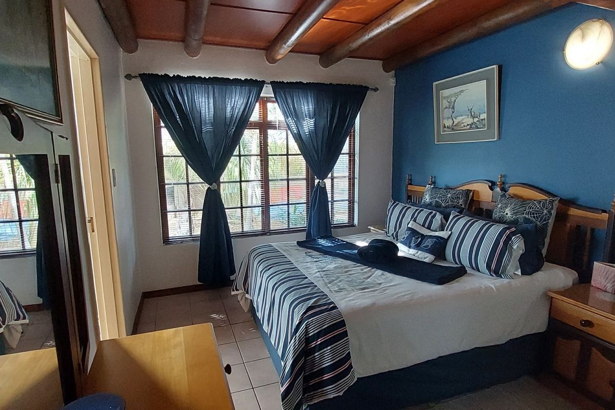 A bedroom featuring exposed timber ceiling beams, tiled flooring, and a large window with security bars.