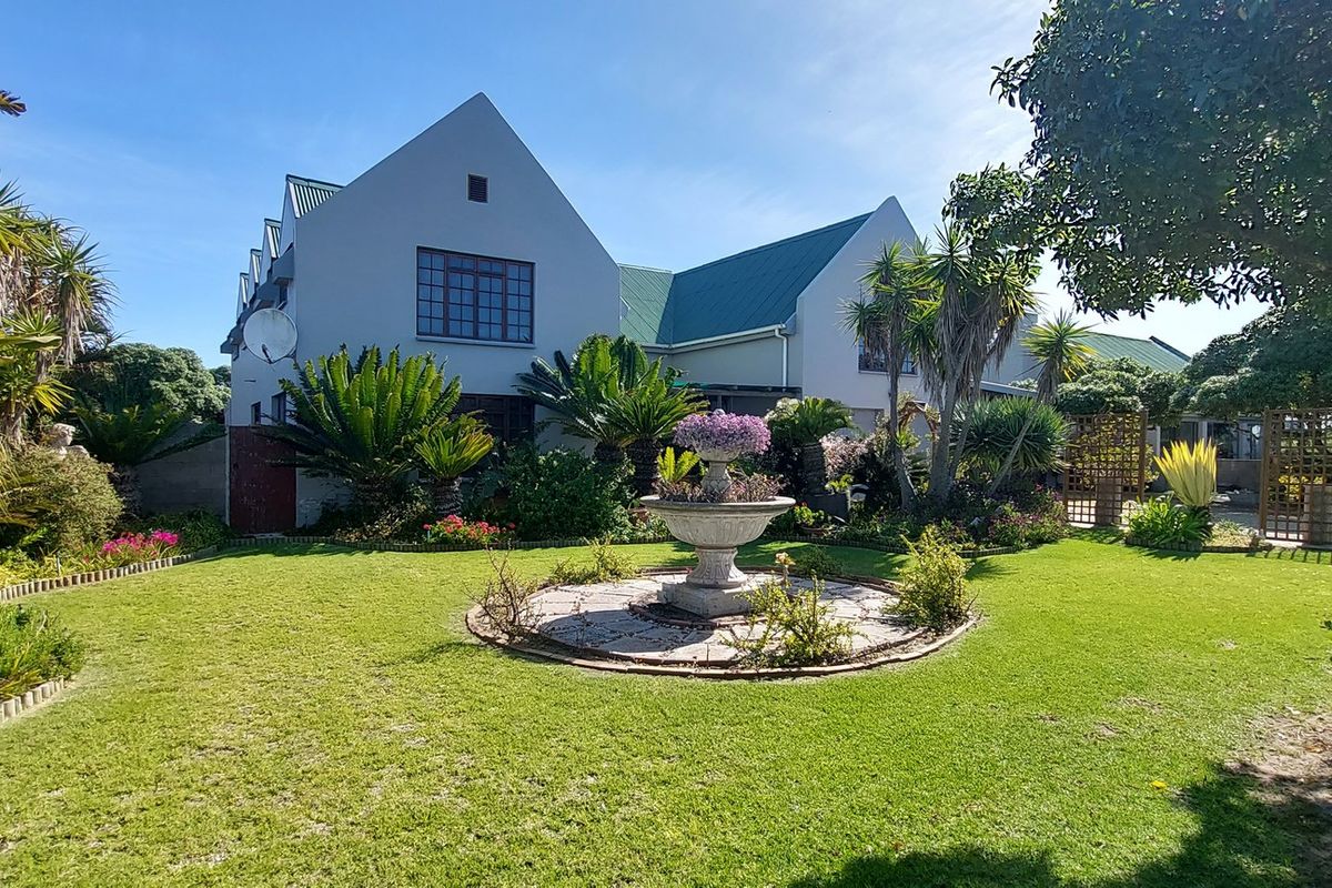 A well-maintained rear garden featuring a central stone fountain, lush lawn, mature landscaping, and a view of the property's rear elevation.